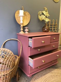 a pink dresser next to a wicker chair and rattan basket on the floor