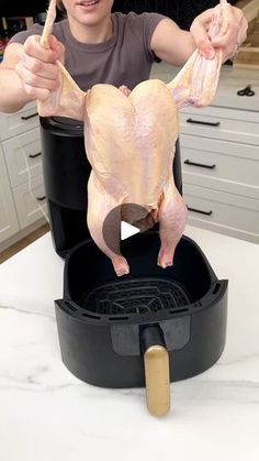 a woman is holding up a whole chicken in her hands while standing over an open roasting pan