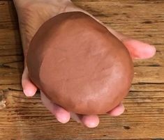 a person is holding a chocolate doughnut in their hand on a wooden table top