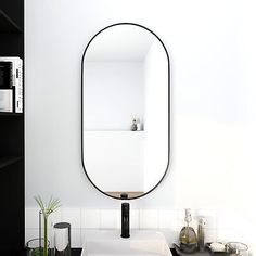 a bathroom sink with a large oval mirror over it's top shelf next to a black and white counter