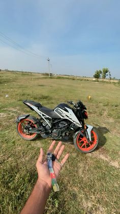 a person is holding up their hand near a motorcycle on the grass with an orange rim