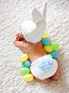 a baby laying on top of a white rug wearing a diaper and bunny hat