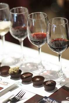 four wine glasses are lined up on a table with chocolates and candies in them