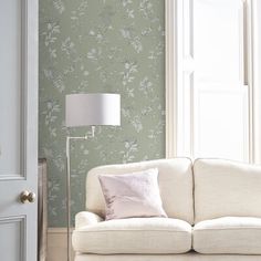 a white couch sitting next to a window in a room with green wallpaper on the walls