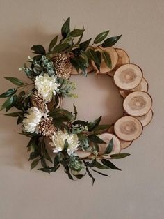 a wreath made out of wood slices with white flowers and greenery on top is hung on the wall