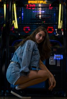 a young woman kneeling down in front of a machine with neon lights on the side