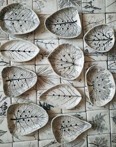 several leaf shaped dishes are arranged on a tile wall with leaves drawn on them in black and white