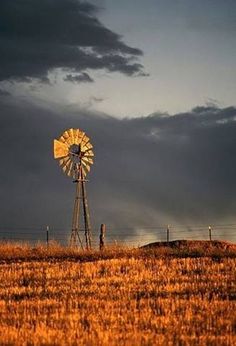 an old windmill in the middle of a field under a cloudy sky with dark clouds