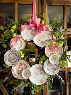 a wreath made out of plates with pink bows hanging from the front and side of it