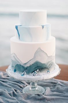 a three tiered white cake with blue and grey frosting on the top layer