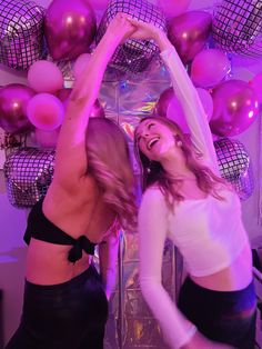 two women dancing in front of purple and pink balloons