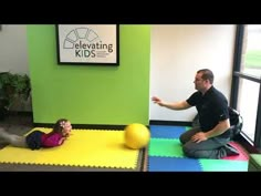 a man sitting on the floor next to a child playing with a ball and another person kneeling down