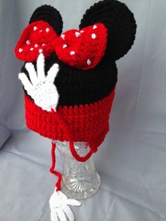 a crocheted mickey mouse hat on top of a clear glass vase with a red bow