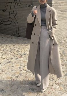 a woman is walking down the street with an umbrella in her hand and wearing a gray coat