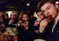 a group of young men eating donuts in front of a table full of cupcakes