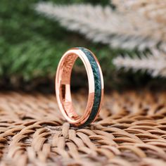 a close up of a wedding ring on a woven surface with pine needles in the background