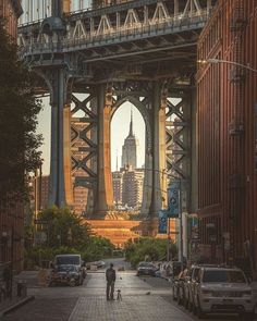 an image of a man walking down the street in front of a bridge with tall buildings