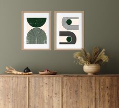 two framed art prints on the wall above a wooden cabinet with plants in vases