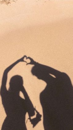 a shadow of a person holding a surfboard on the beach with their hands in the shape of a heart