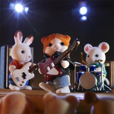 three toy mice are playing music on the stage with guitars and bassets in front of them