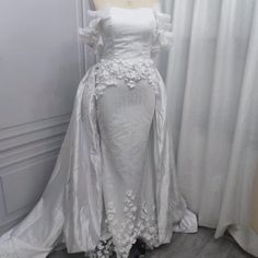 a white wedding dress on display in front of a window with curtains and drapes