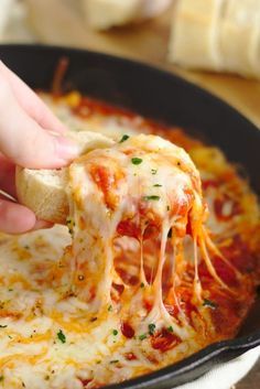 someone is dipping cheese into a skillet filled with lasagna sauce and melted cheese