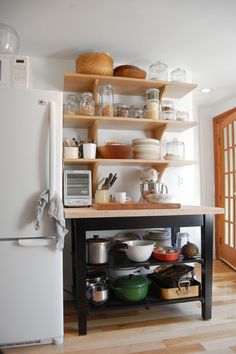 a kitchen with shelves filled with pots and pans next to a refrigerator freezer