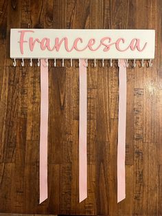 a wooden wall with pink ribbon hanging from it's sides and the word francesa written on it