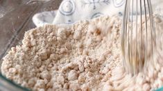 a whisk in a glass bowl filled with flour next to a blue and white towel