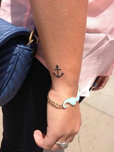 a woman with a small anchor tattoo on her wrist and hand holding a blue purse