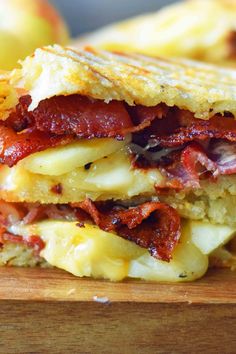 a bacon and cheese sandwich cut in half on a cutting board next to an apple