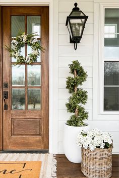 the front door is decorated with wreaths and potted planters on the porch