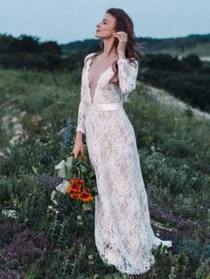 a woman in a long white dress is standing in the grass and holding a bouquet