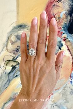 a woman's hand with a diamond ring on top of her left hand, in front of a painting