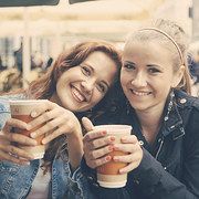 two young women are smiling and holding coffee cups