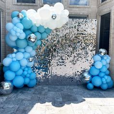 blue and white balloons in front of a building with silver balls on the ground next to it