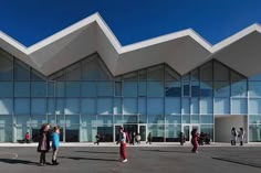 people are walking around in front of a building with glass walls and triangular shaped windows