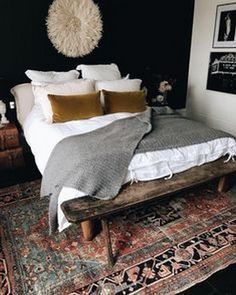 a bed with pillows and blankets on top of it next to a wooden bench in front of a black wall