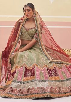 Introducing the Mehendi Green Silk Bridal Lehenga, a masterpiece of elegance and tradition. This stunning bridal lehenga features intricate zardozi embroidery with silken threads, dabka, cutdana, and sequins underlayed with multi colored velvet appliques. The green raw silk blouse perfectly complements the lehenga, while the double dupatta in matching green and contrasting crimson adds a touch of opulence. Make your wedding day truly unforgettable with this exquisite bridal wedding dress. Composition : Lehenga and Blouse - Raw Silk, Dupatta - Soft Net Care: Dry Clean Only and Vacuum Storage This product can be customized for sleeves, length of blouse and neckline Delivery : 2-4 weeks as the product is hand crafted. Check Size Guide or choose MySize for free customisation (All Sizes above X Pista Green Chanderi Choli With Intricate Embroidery, Intricate Embroidered Pista Green Chanderi Choli, Pista Green Raw Silk Choli With Intricate Embroidery, Festive Dola Silk Lehenga With Intricate Embroidery, Dola Silk Lehenga With Zari Work For Traditional Ceremonies, Wedding Lehenga With Intricate Embroidery In Jamawar, Jamawar Lehenga For Wedding With Traditional Drape, Unstitched Anarkali Lehenga In Jamawar, Festive Anarkali Lehenga In Jamawar