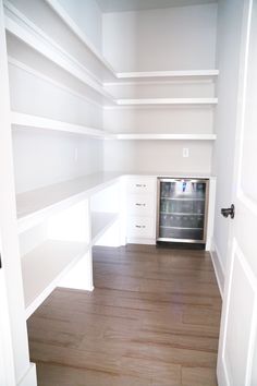 an empty room with white shelving and wood flooring in the corner, looking into the kitchen