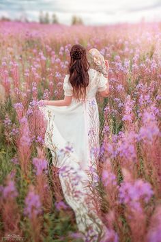 a woman walking through a field of purple flowers with her back to the camera,