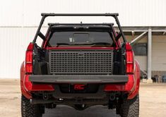 the back end of a red truck parked in front of a building with white walls