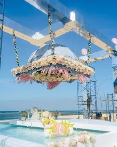 an outdoor wedding setup with flowers hanging from the ceiling and chairs on the beach in the background