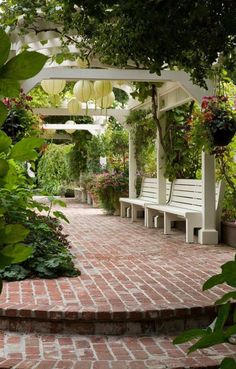 a white bench sitting on top of a brick walkway next to trees and flowers in pots