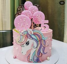 a birthday cake decorated with pink frosting and a unicorn head on the top is surrounded by balloons