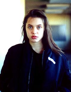 a young woman standing next to a wall wearing a black jacket and white t - shirt