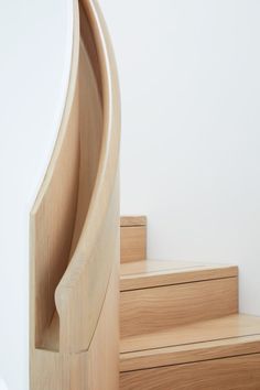 a close up of a wooden stair case on a white wall with stairs in the background