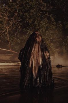 a woman standing in the water with her back turned to the camera, wearing a long black dress