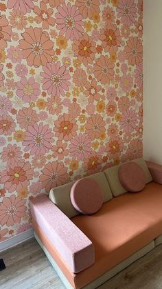 an orange and pink couch in front of a wall with flowers on the wall behind it