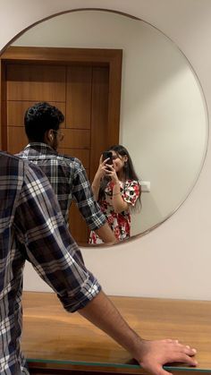 a man taking a photo of a woman in the mirror with her cell phone while she takes a selfie